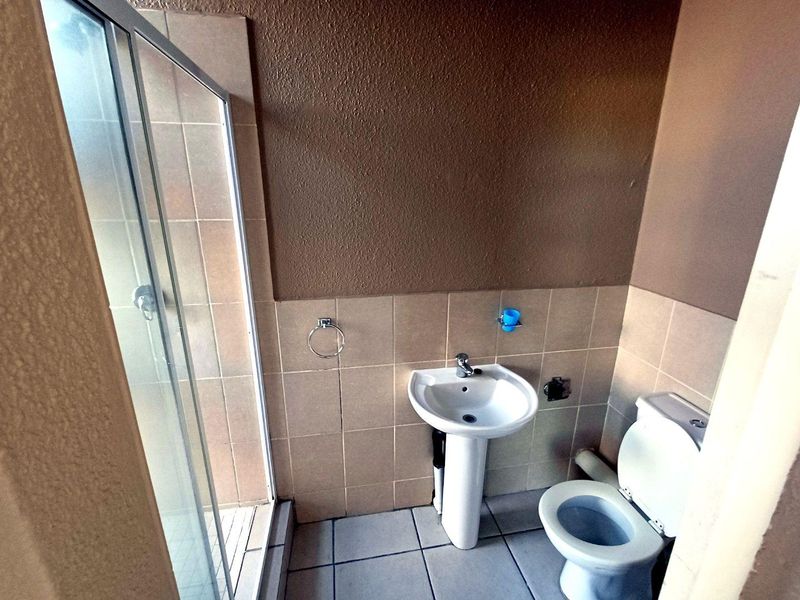A functional bathroom featuring a pedestal basin, toilet, and a glass-enclosed shower with neutral wall and floor tiling.