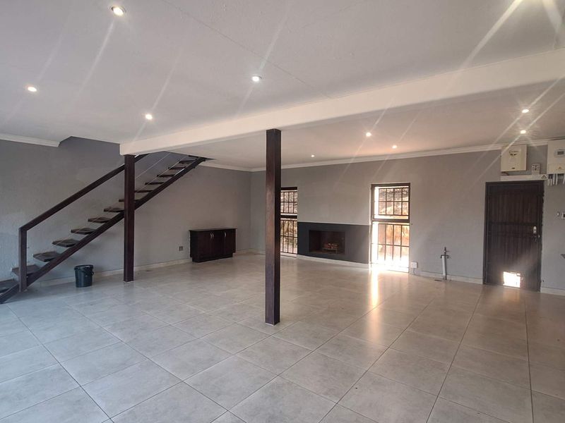 Spacious open-plan living area featuring tiled floors, a built-in fireplace, a staircase, and a functional kitchen with integrated appliances.