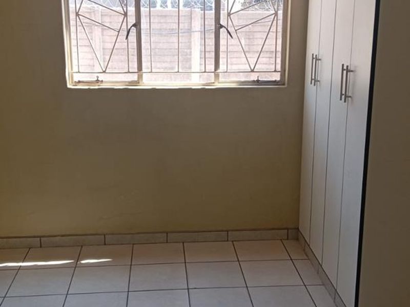 A vacant bedroom featuring tiled flooring, built-in cupboards, and a window fitted with security bars.