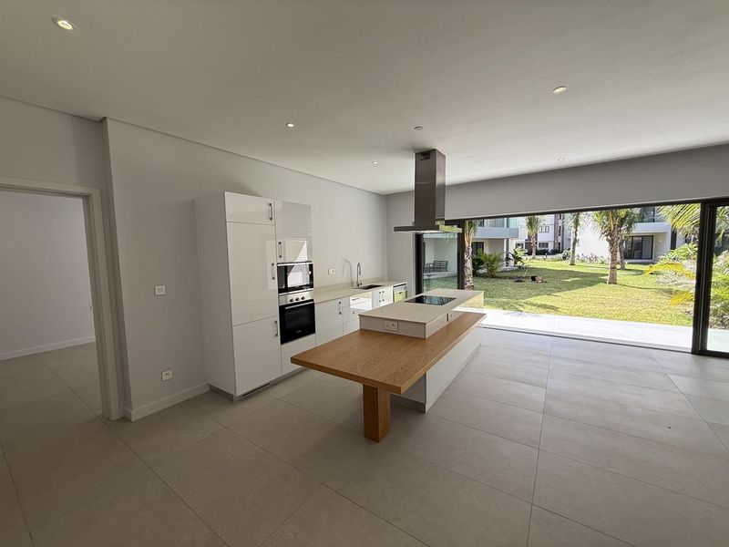 Modern open-plan kitchen featuring a central island with integrated hob, built-in appliances, and seamless access to the garden through large sliding glass doors.