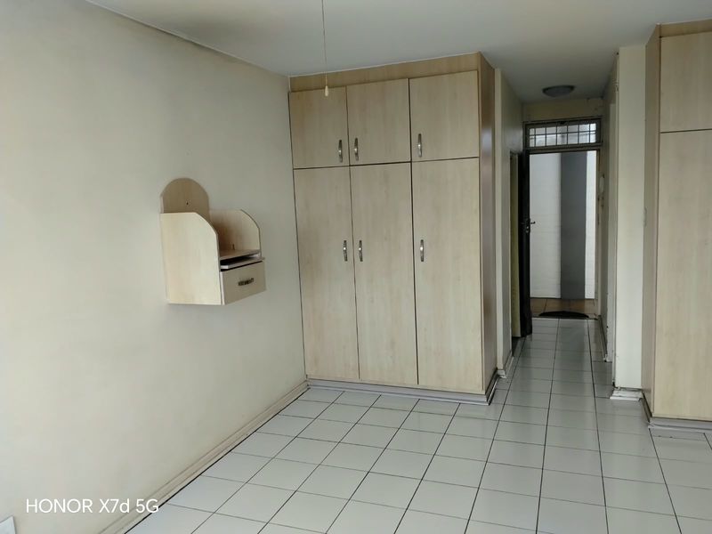 A vacant bedroom featuring light wood-finish built-in cupboards, white tiled flooring, and a wall-mounted storage unit.