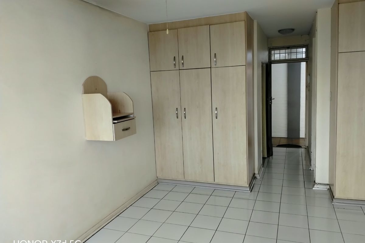 A vacant bedroom featuring light wood-finish built-in cupboards, white tiled flooring, and a wall-mounted storage unit.
