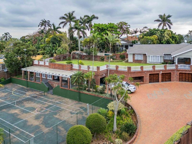 Aerial view of a large residential property featuring a private tennis court, extensive brick driveway, triple garage, and a raised terrace area.
