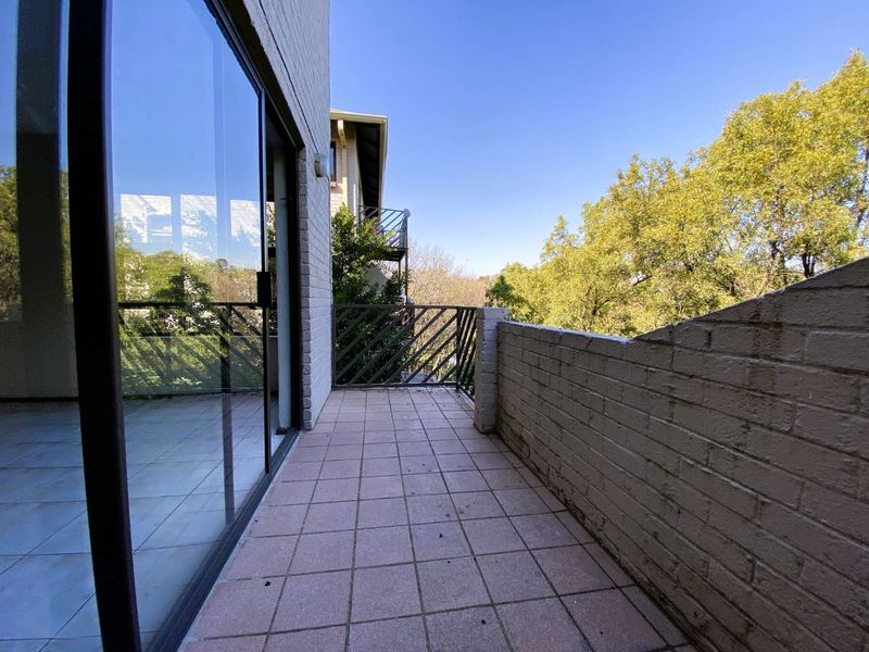 A private balcony featuring tiled flooring, a brick parapet wall, and a metal balustrade, accessible via a large sliding glass door.