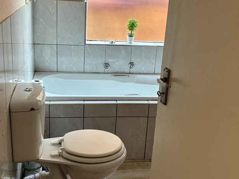 A functional bathroom featuring a bathtub, toilet, and tiled finishes. The space would benefit from cosmetic updates to modernize the fixtures and finishes.