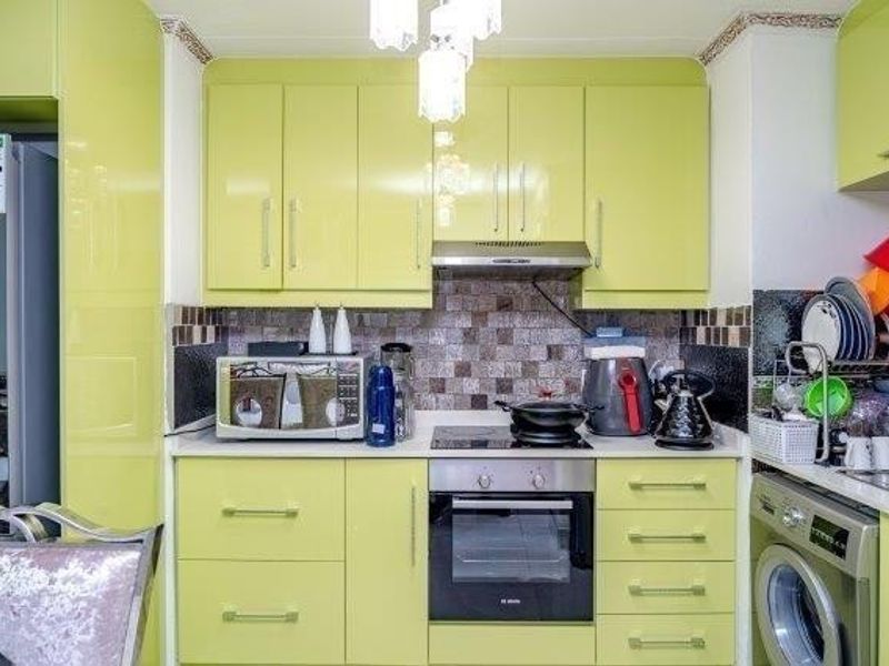 A compact kitchen featuring lime green cabinetry, mosaic tile backsplash, built-in oven, electric hob, extractor fan, and an integrated washing machine.