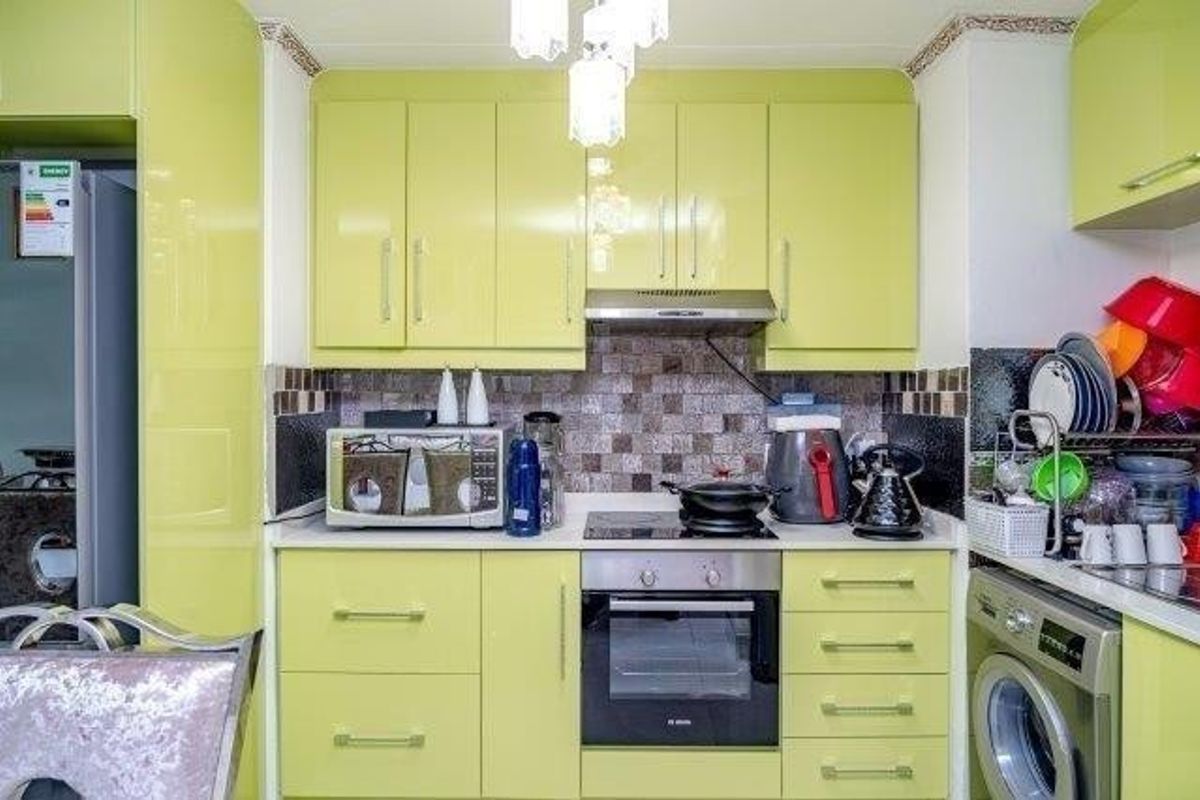 A compact kitchen featuring lime green cabinetry, mosaic tile backsplash, built-in oven, electric hob, extractor fan, and an integrated washing machine.
