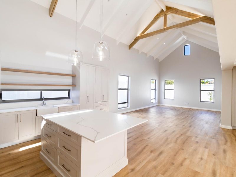 Spacious open-plan living area featuring a high vaulted ceiling with exposed timber trusses, modern kitchen with island, and light wood-look flooring.