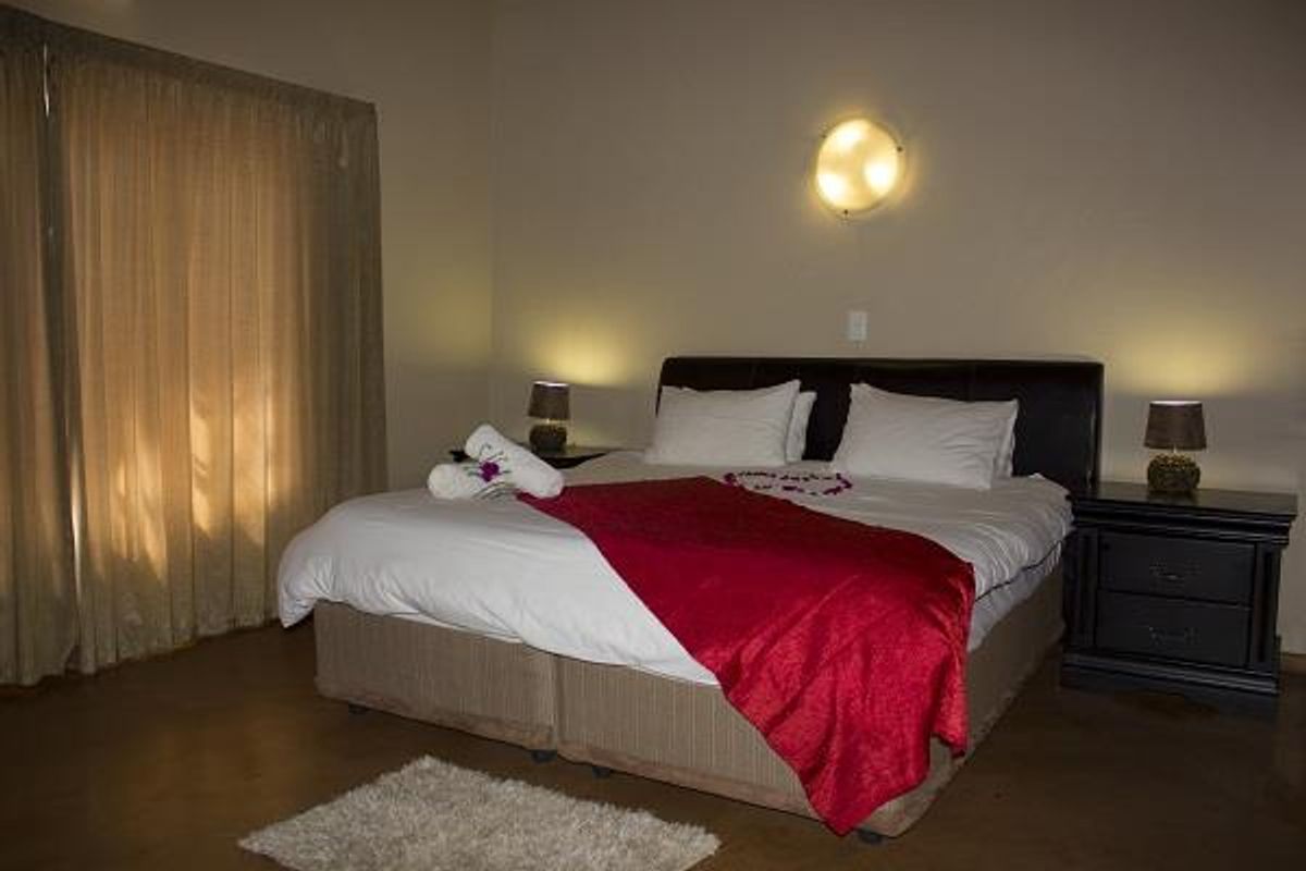 A comfortable bedroom featuring neutral wall tones, warm wall-mounted lighting, and floor-length curtains.