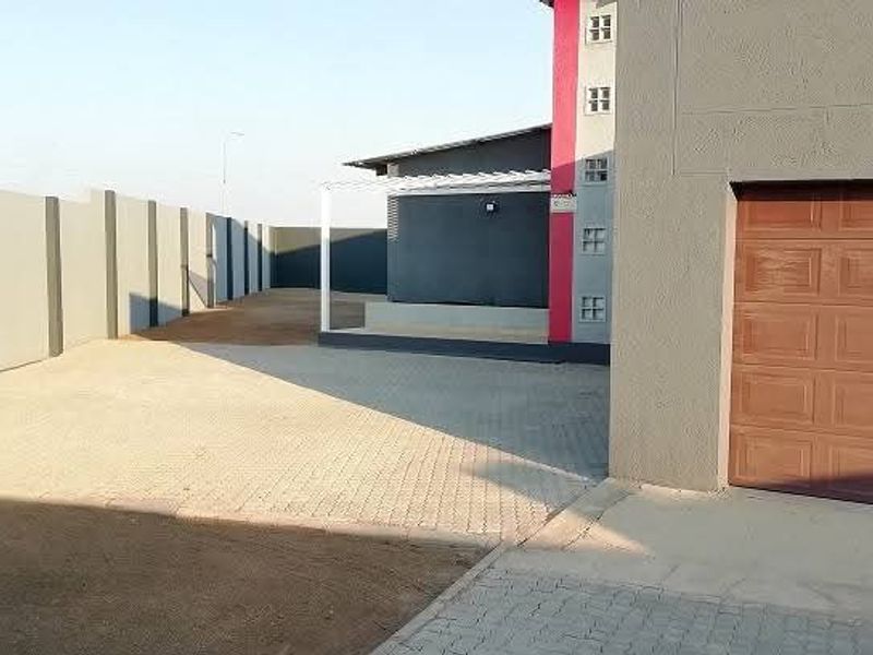 A view of the property exterior featuring a paved driveway, perimeter wall, and a single garage door with an adjacent covered patio area.
