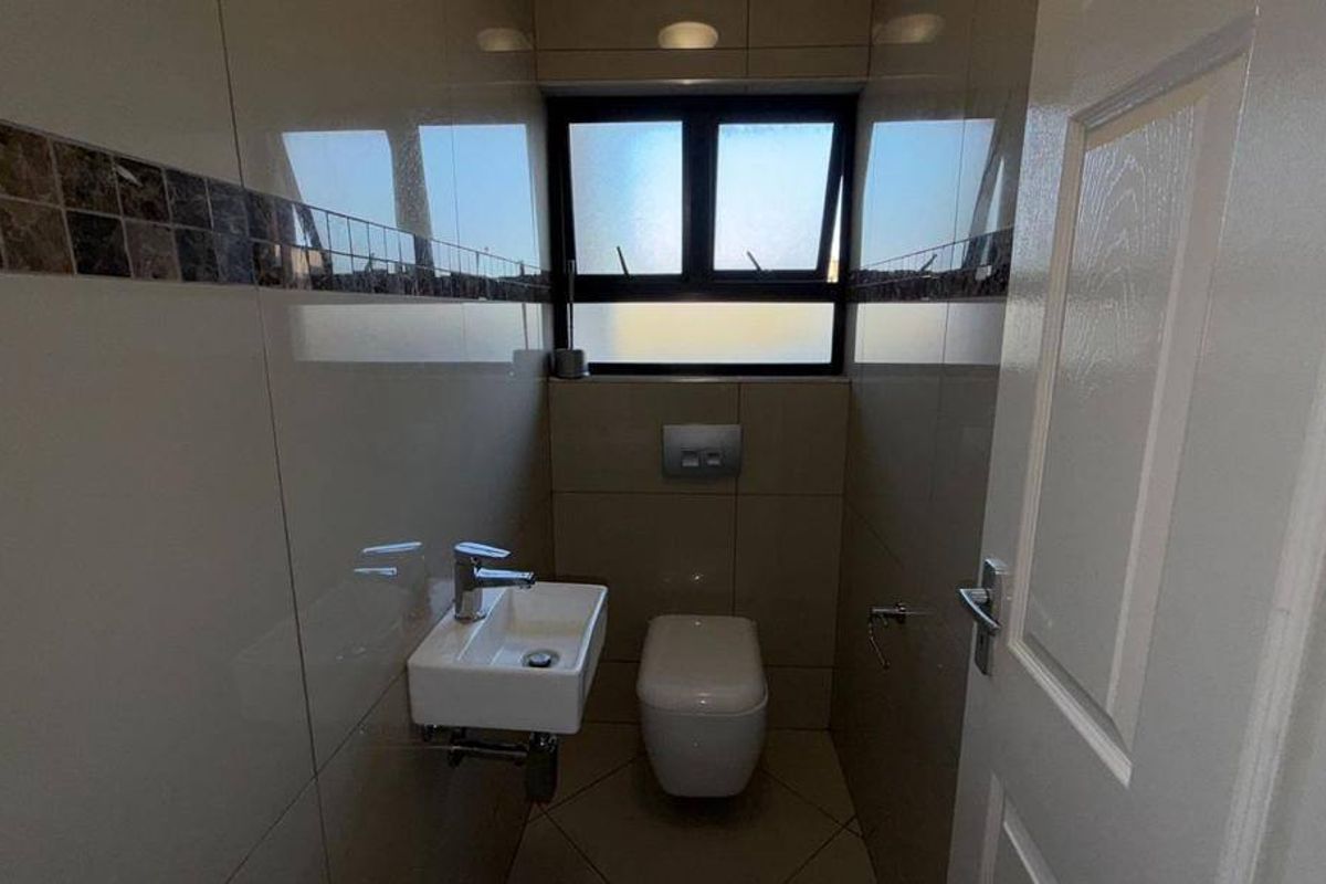 A compact, modern guest bathroom featuring floor-to-ceiling tiled walls, a wall-mounted basin, and a concealed cistern toilet.