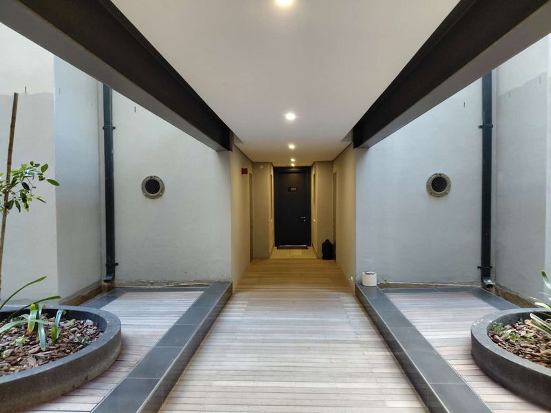 A modern, covered walkway featuring timber decking, recessed lighting, and circular architectural windows, leading to a private apartment entrance.