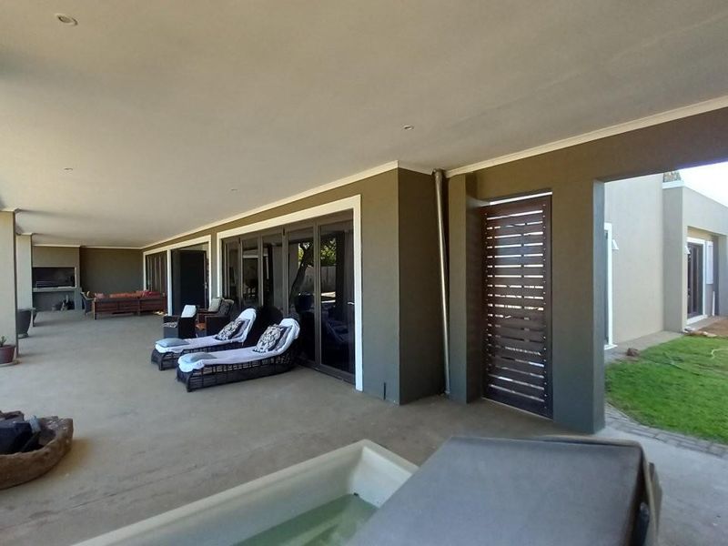 Spacious covered patio featuring concrete flooring, built-in braai area, and direct access to the garden through large sliding glass doors.