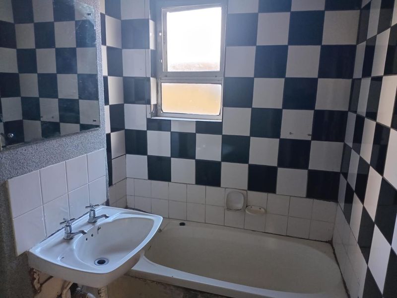 A dated bathroom featuring a bathtub, pedestal basin, and distinctive black and white checkered wall tiling, requiring cosmetic updates to modernize the space.