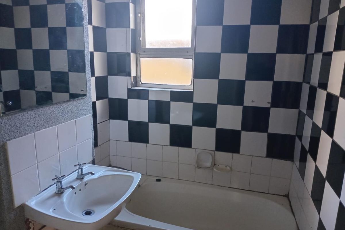 A dated bathroom featuring a bathtub, pedestal basin, and distinctive black and white checkered wall tiling, requiring cosmetic updates to modernize the space.
