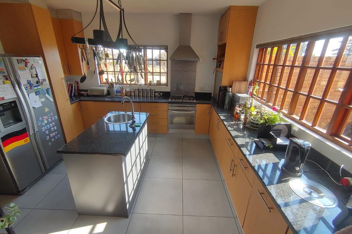 A functional kitchen featuring wooden cabinetry, granite countertops, a central island with a prep sink, and a stainless steel oven with an extractor fan.