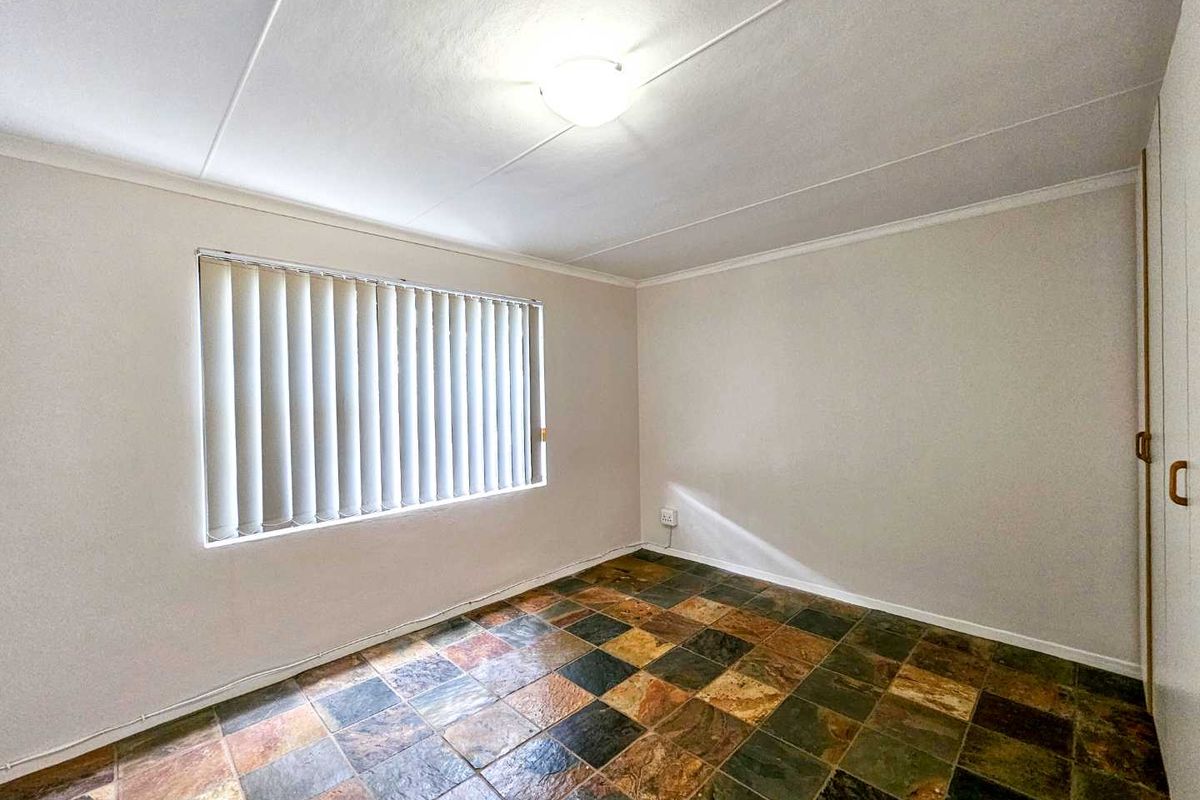 A clean, empty bedroom featuring slate tile flooring, vertical blinds, and built-in wardrobe storage.