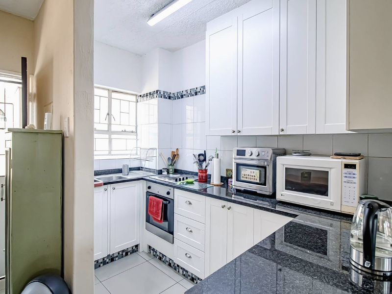 Compact kitchen featuring white cabinetry, granite countertops, built-in oven, and tiled backsplash with a functional layout.