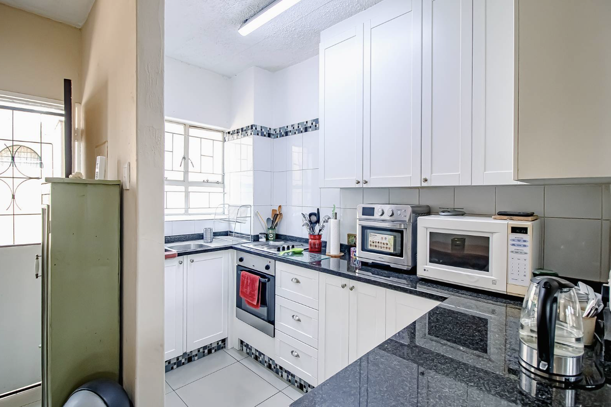 Compact kitchen featuring white cabinetry, granite countertops, built-in oven, and tiled backsplash with a functional layout.