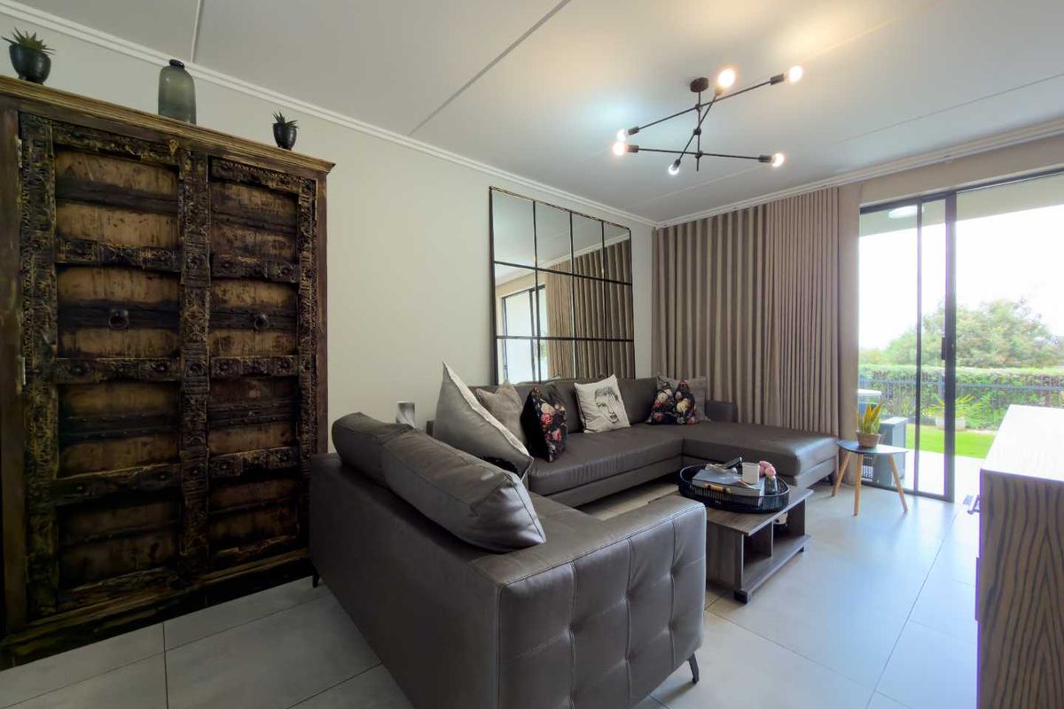 A bright and modern living room featuring large format floor tiles, a contemporary chandelier, and sliding glass doors leading to an outdoor patio area.