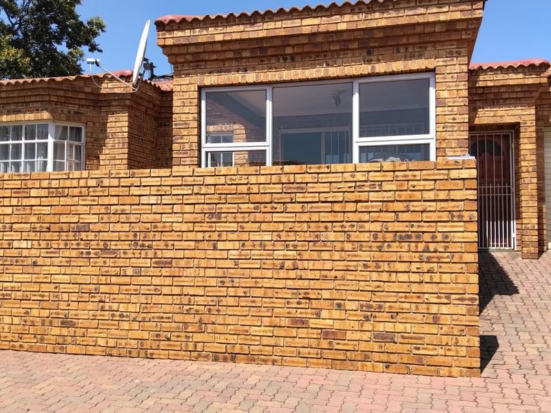 Front elevation of a face brick townhouse featuring a paved driveway, secure garage access, and a private boundary wall.