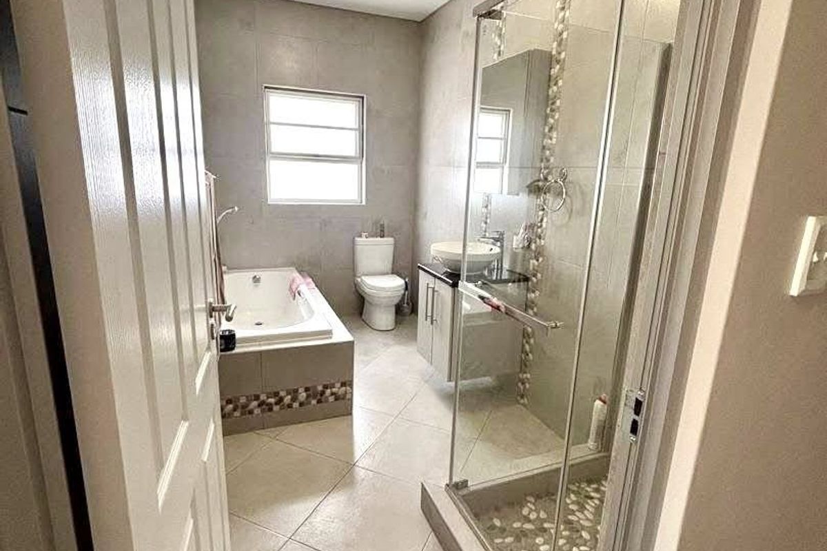 Modern bathroom featuring a glass-enclosed shower, a built-in bathtub, a vanity with a vessel sink, and neutral floor-to-ceiling tiling.
