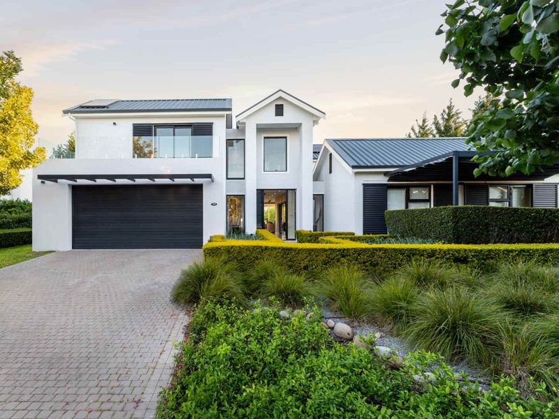 Modern two-story residential home featuring a double garage, clean white facade, metal roofing, and a well-maintained landscaped front garden with paved driveway.