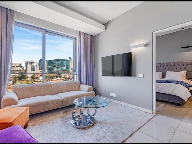 Modern living room featuring large sliding glass doors with city views, tiled flooring, and recessed lighting, with an adjacent bedroom visible.