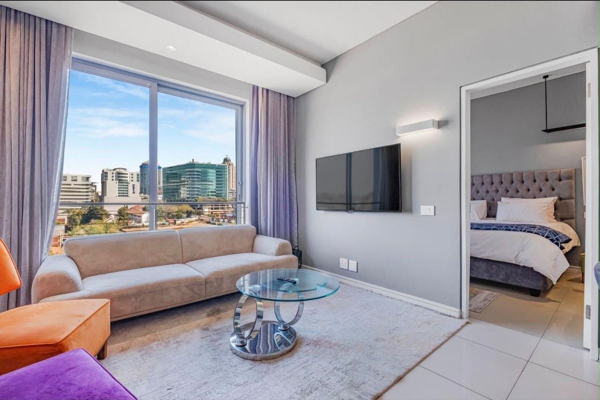 Modern living room featuring large sliding glass doors with city views, tiled flooring, and recessed lighting, with an adjacent bedroom visible.