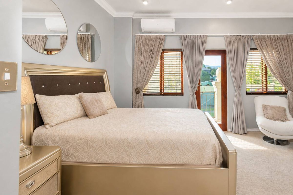 A well-maintained bedroom featuring neutral tones, split-system air conditioning, recessed lighting, and direct access to a private balcony through a timber-framed glass door.