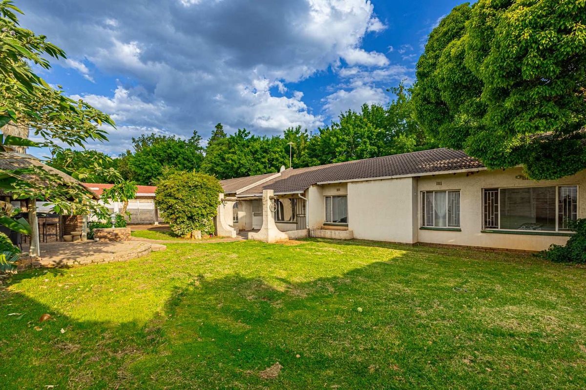Spacious rear garden featuring a large lawn, paved patio area, and a thatched lapa, providing a functional outdoor entertainment space.