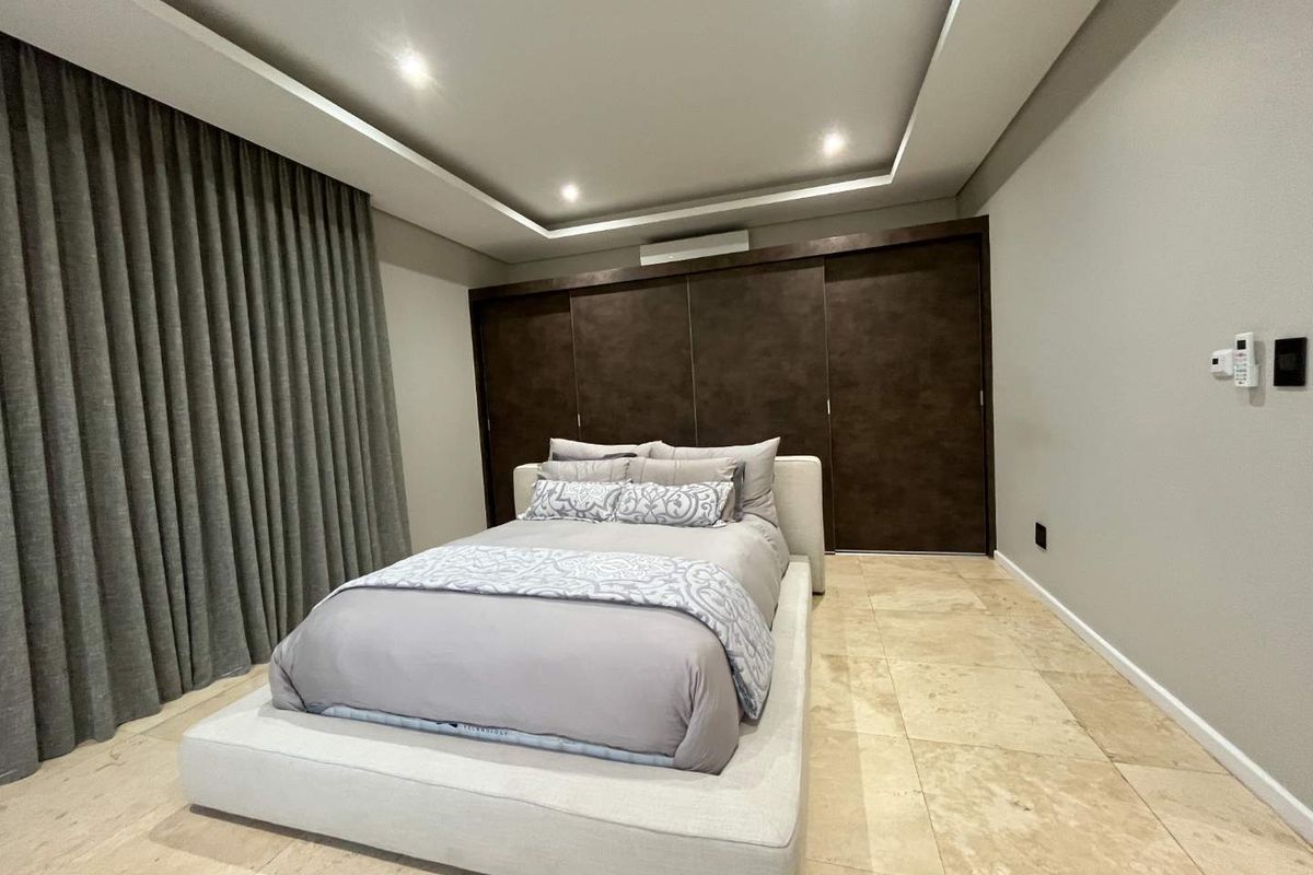 Modern bedroom featuring stone floor tiles, recessed ceiling with downlights, built-in wardrobe, and a split-system air conditioner.