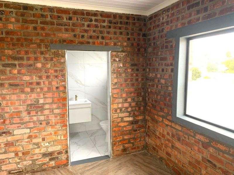 A bedroom featuring exposed brick walls, laminate flooring, and an en-suite bathroom with modern white tiling.