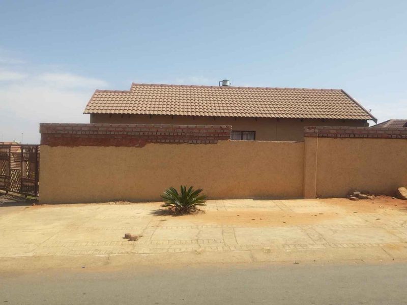 Front exterior view of a residential property featuring a tiled roof, perimeter wall with unfinished brickwork, and a concrete driveway.