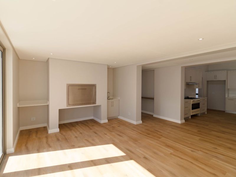 Spacious open-plan living area featuring light laminate flooring, a built-in braai, and a modern kitchen with integrated appliances and ample cabinetry.
