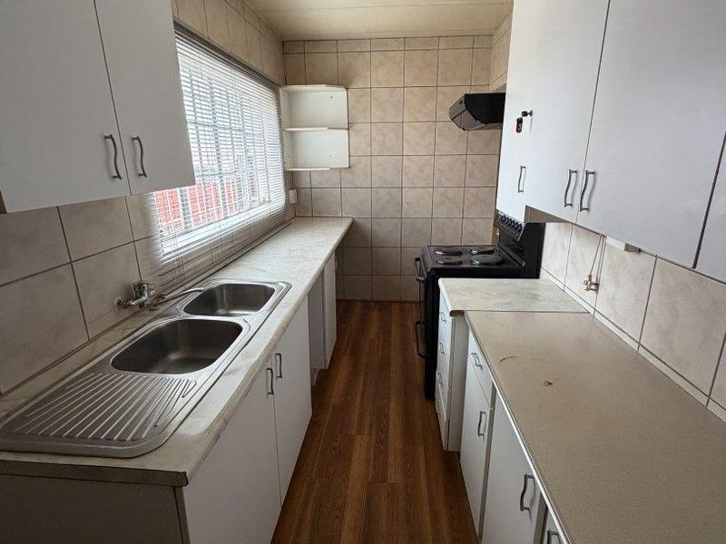 A functional galley-style kitchen featuring white cabinetry, laminate countertops, a double stainless steel sink, and a freestanding stove with an extractor fan.