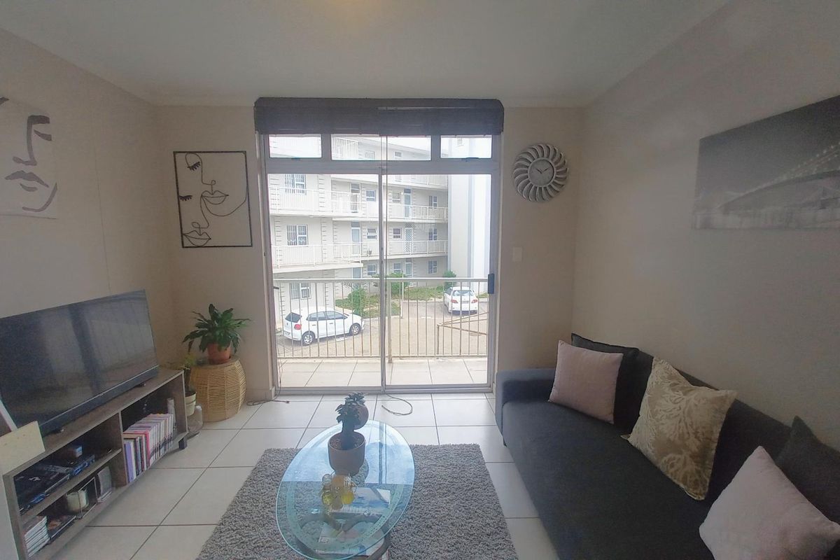 A living room featuring tiled flooring and a large sliding glass door that provides access to an outdoor balcony area.