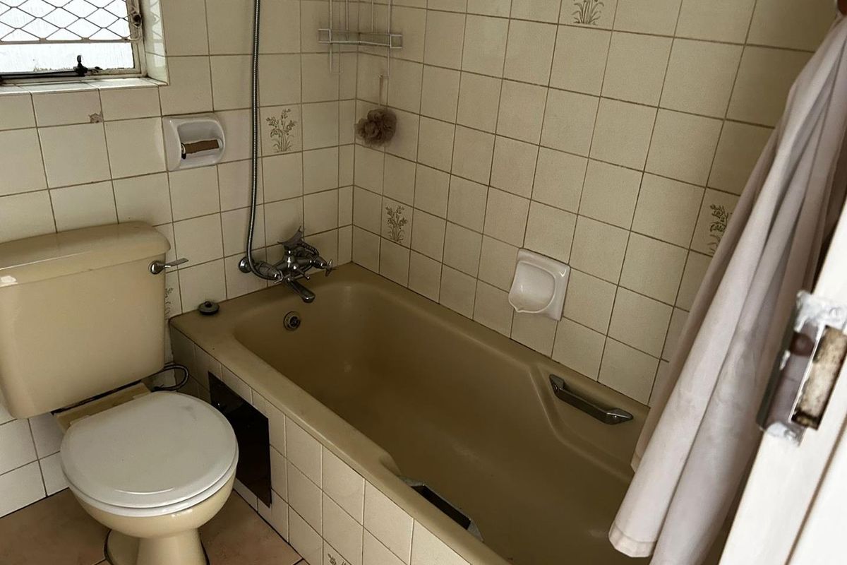 A dated bathroom featuring a beige bathtub, matching toilet, and tiled walls with a window for natural light.