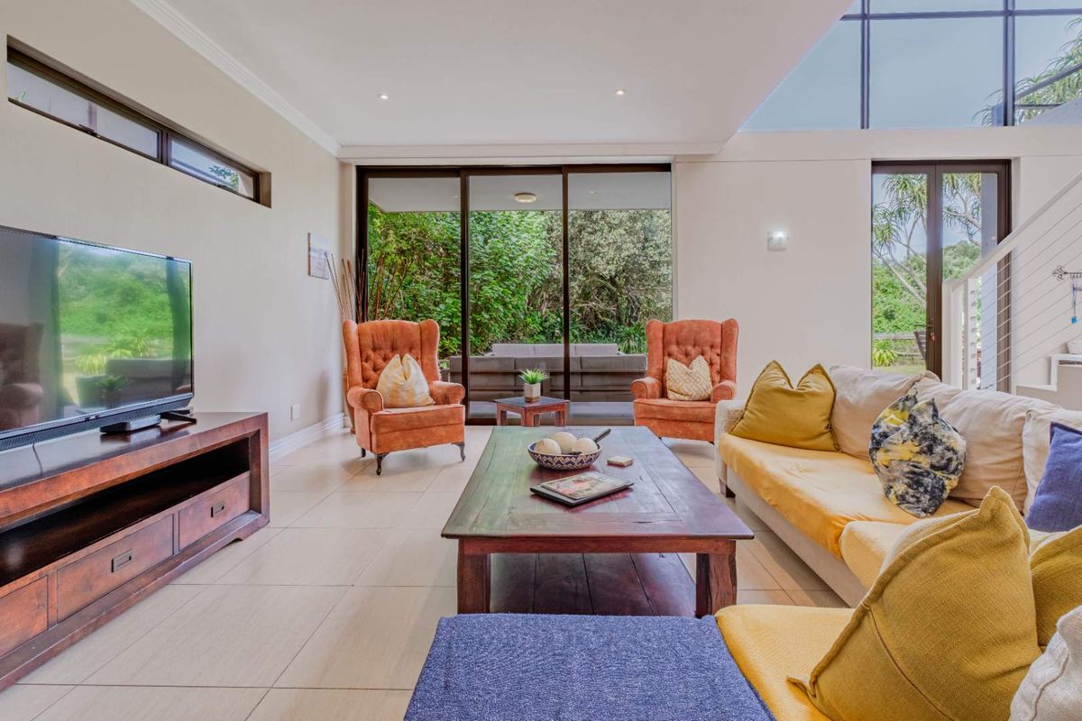 Spacious living room featuring large sliding glass doors, high ceilings with clerestory windows, and neutral tiled flooring, offering seamless access to the outdoor patio area.