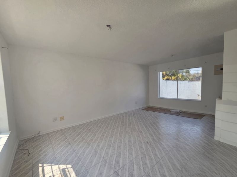 An empty, open-plan living area featuring tiled flooring, large windows, and exposed electrical wiring, ready for renovation or staging.