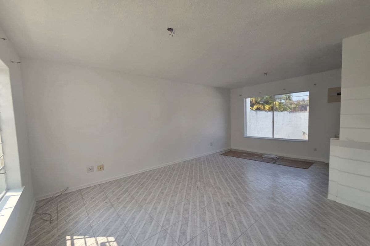 An empty, open-plan living area featuring tiled flooring, large windows, and exposed electrical wiring, ready for renovation or staging.