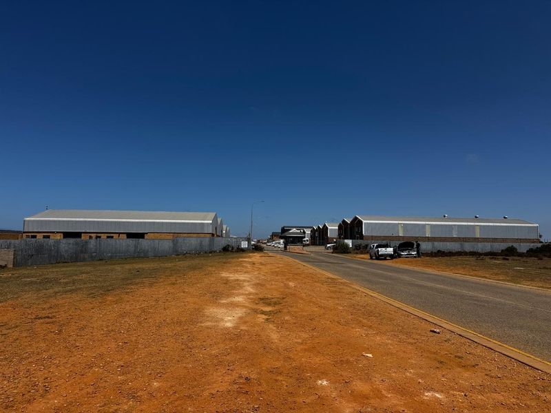 Street view of an industrial park entrance featuring multiple warehouse structures, perimeter fencing, and a security gatehouse.