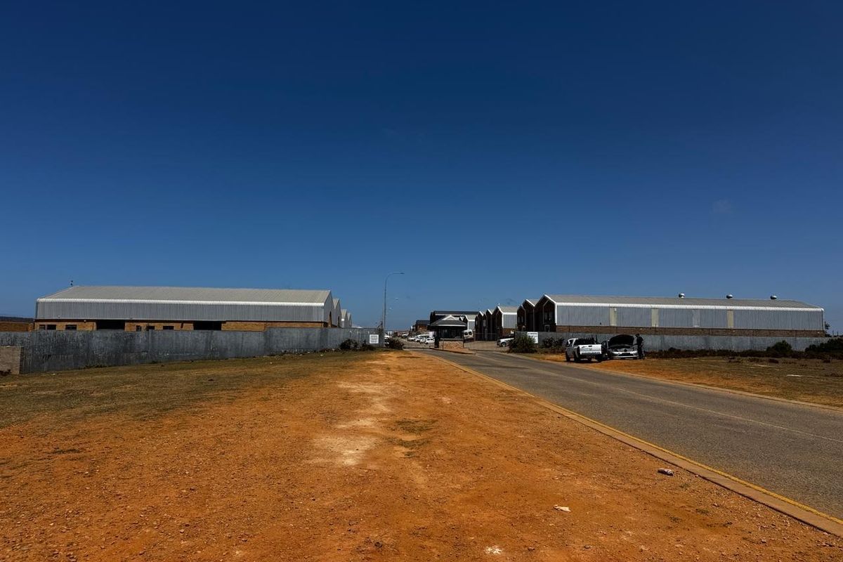 Street view of an industrial park entrance featuring multiple warehouse structures, perimeter fencing, and a security gatehouse.