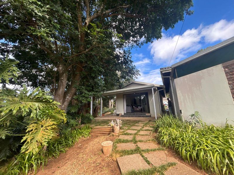 Rear view of the townhouse featuring a covered patio, sliding glass doors, and a landscaped garden with mature trees and paved walkway.