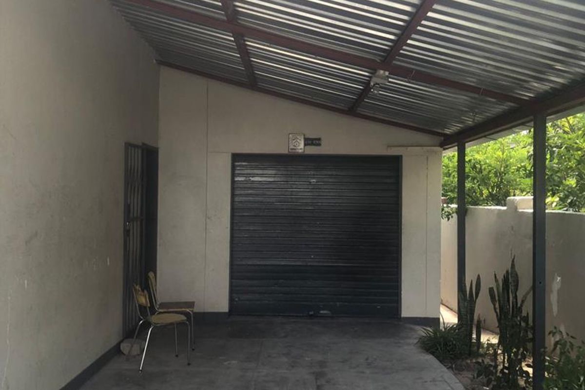 A covered carport area featuring a corrugated metal roof, concrete flooring, and a secure roller shutter garage door.