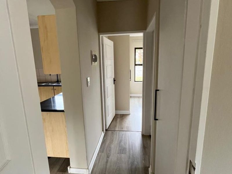 A bright hallway featuring modern laminate flooring and an arched transition leading into the kitchen area.