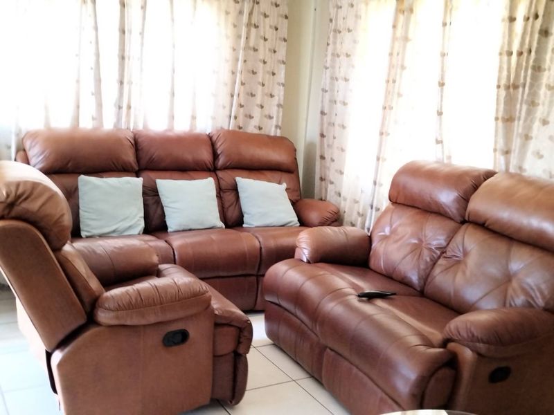A living room area featuring neutral tiled flooring and large windows dressed with curtains.