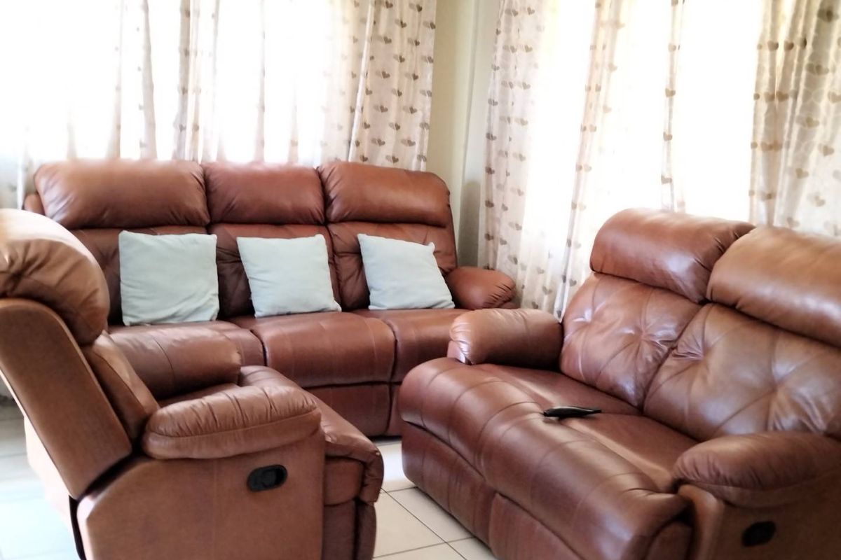 A living room area featuring neutral tiled flooring and large windows dressed with curtains.