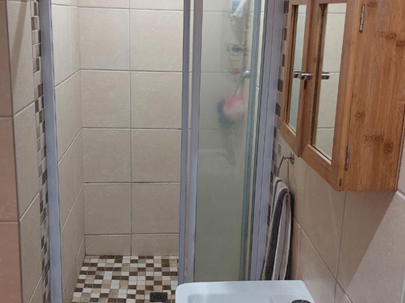 Compact bathroom featuring a tiled shower enclosure, wall-mounted basin with mixer tap, and neutral wall tiling with mosaic accents.