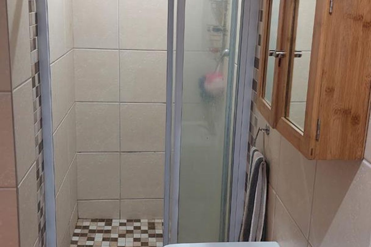 Compact bathroom featuring a tiled shower enclosure, wall-mounted basin with mixer tap, and neutral wall tiling with mosaic accents.